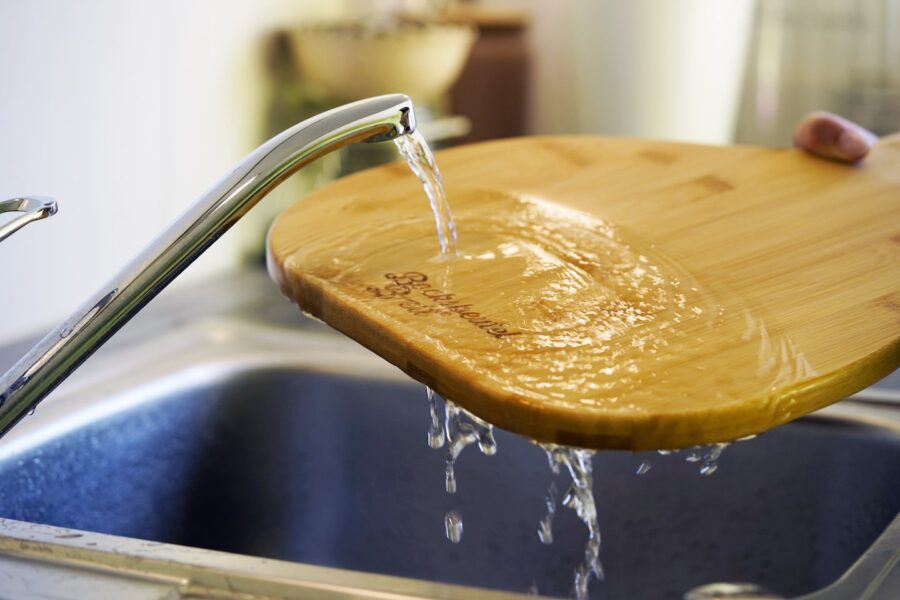 Küchenbrett unter einem fließenden Wasserhahn.